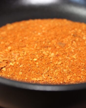 Épices rouges moulues dans un bol noir, prêtes pour une recette épicée et savoureuse.