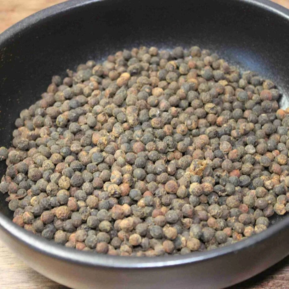 Grains de poivre noir dans un bol, prêts à être moulus pour assaisonner et relever vos plats culinaires.