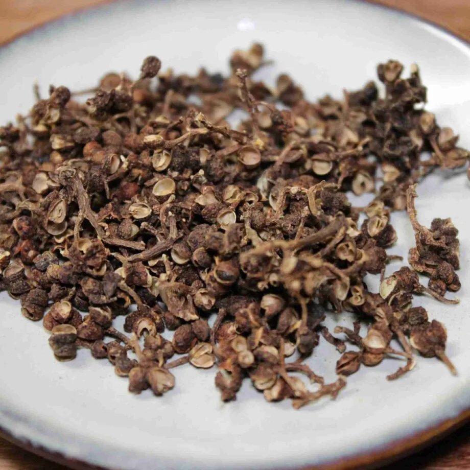 Grains de poivre de Sichuan séchés sur une assiette, épice asiatique au goût unique et piquant.