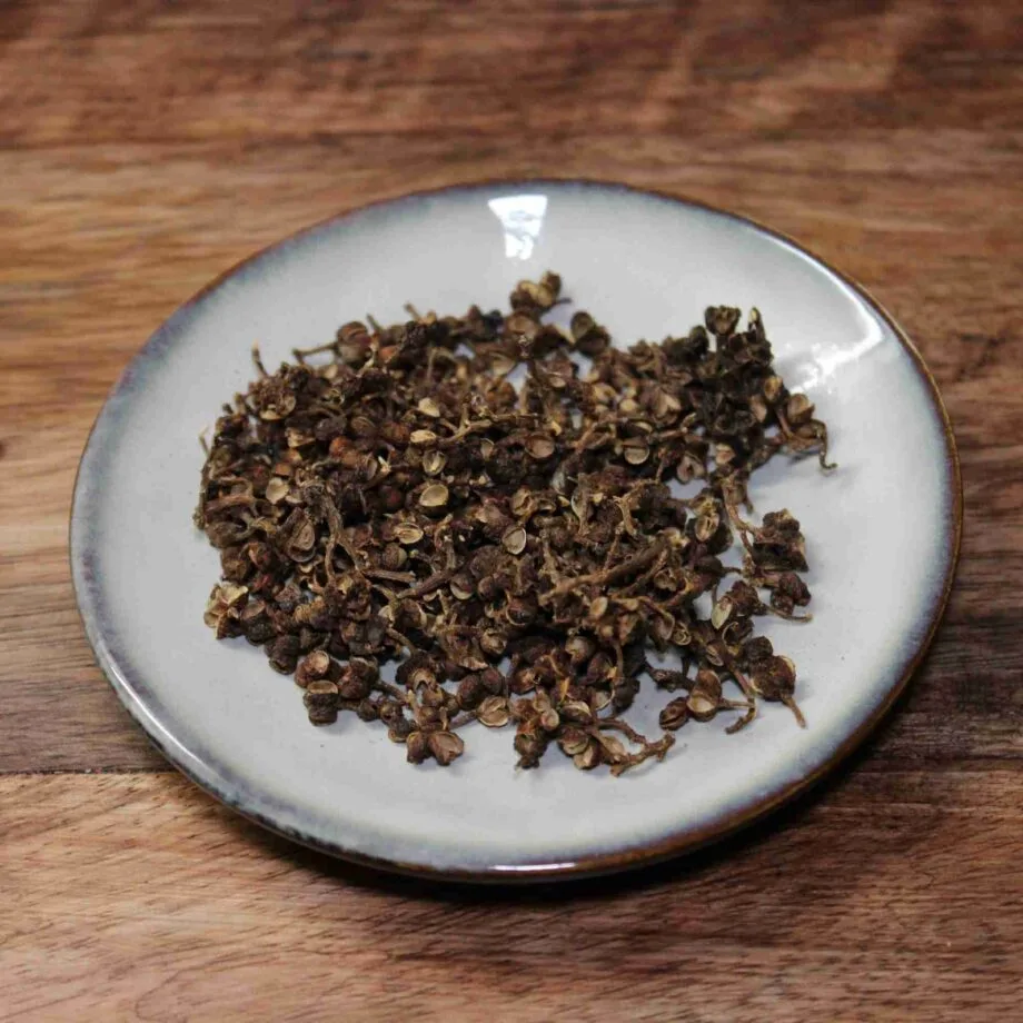 Baies de Sichuan séchées sur une assiette blanche, posée sur une table en bois.