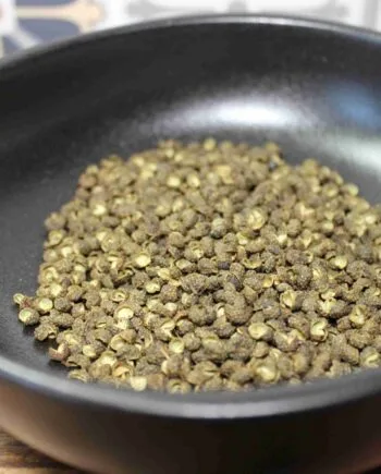 Grains de poivre de Sichuan dans un bol noir, prêt pour assaisonnement et plats épicés.