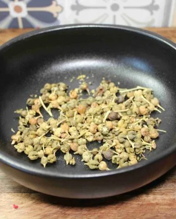 Graines d'ashwagandha séchées dans un bol noir sur une table en bois.