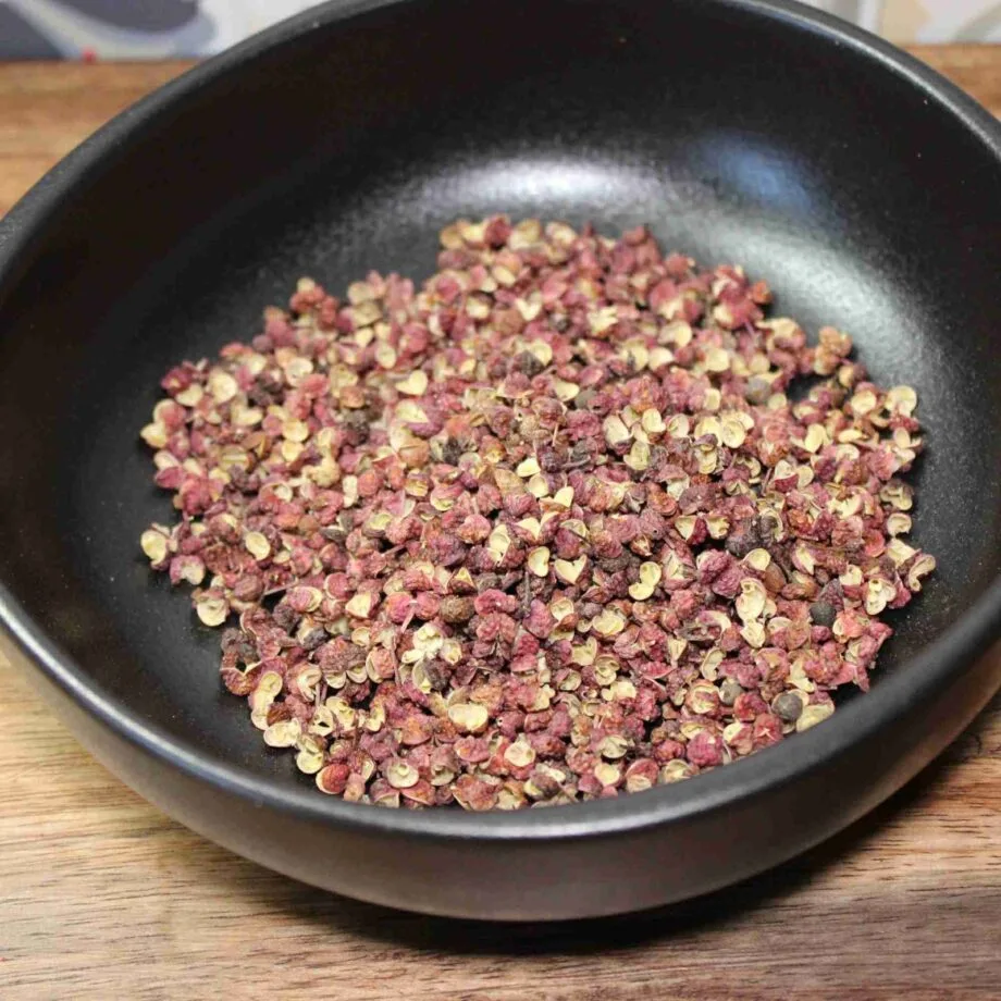 Grains de poivre de Sichuan dans un bol noir sur une table en bois, prêts à être utilisés en cuisine asiatique.