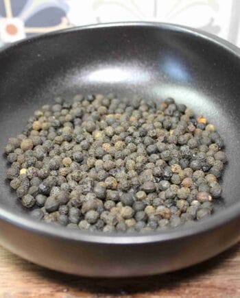 Grains de poivre noir dans un bol en céramique noire, épice aromatique pour la cuisine.