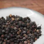 Baies séchées épicées sur assiette blanche, idéal pour assaisonner plats exotiques et créoles.