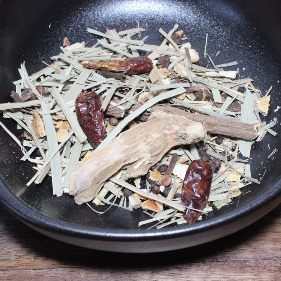 Mélange d'épices et herbes séchées dans un bol noir, idéal pour infusions ou plats aromatiques.