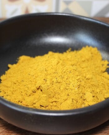 Poudre d'épices jaune vif dans un bol noir, idéale pour la cuisine exotique et recettes savoureuses.