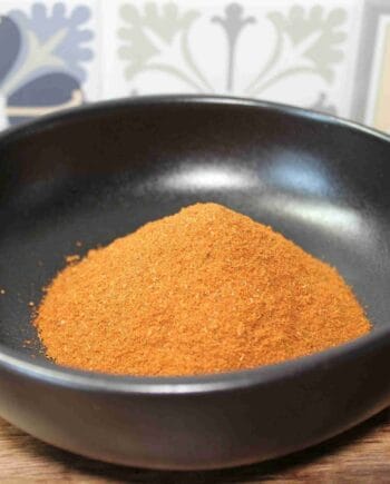 Poudre d'épices orange dans un bol noir, sur fond de motifs floraux.