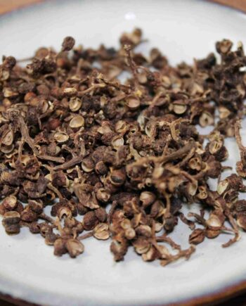 Grains de poivre de Sichuan séchés sur une assiette, épice asiatique au goût unique et piquant.