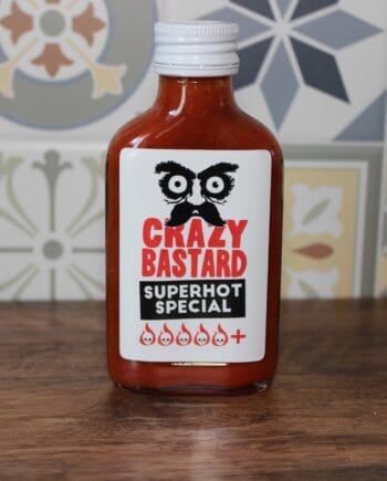 Bouteille de sauce piquante Crazy Bastard Superhot Special sur fond de carrelage coloré.