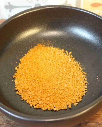 Granules d'oignon séché dans un bol noir sur fond de carreaux colorés.