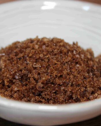 Bol de sucre brun naturel en gros grains sur un fond de céramique blanche.