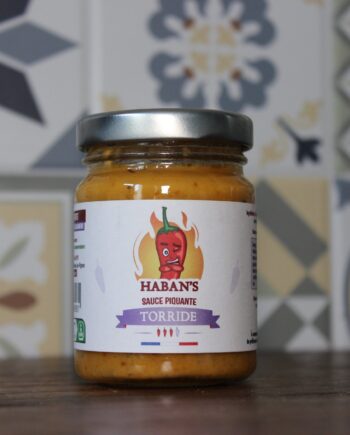 Bocal de sauce piquante Haban's Torridé sur fond de carreaux décoratifs colorés. Parfait pour relever vos plats.