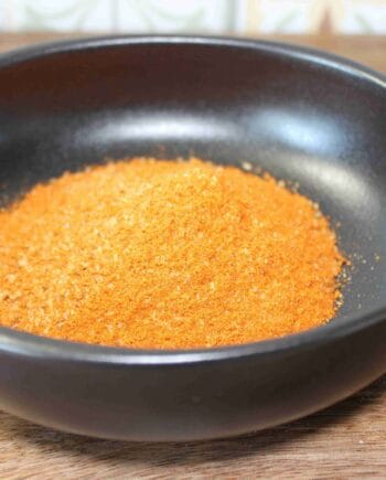 Assaisonnement orange vif dans un bol noir, idéal pour relever vos plats et recettes préférées.