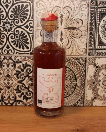 Bouteille de vinaigre artisanal sur fond de carreaux en céramique ornés de motifs noirs et blancs.