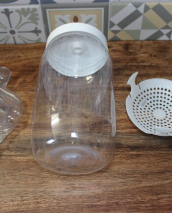 Kit de fermentation maison : bocal en plastique, couvercle spécial et panier filtre sur un plan de travail en bois.