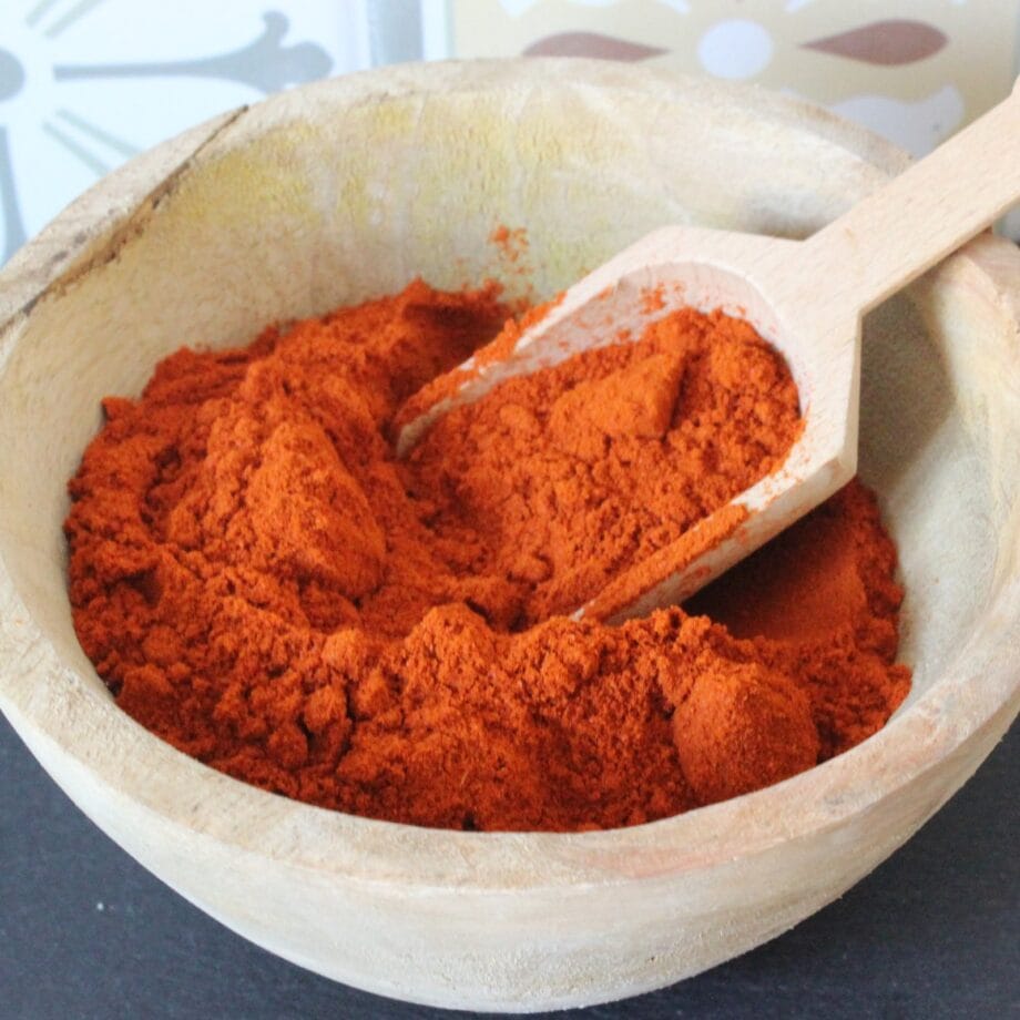 Bol en bois rempli de paprika rouge en poudre avec une cuillère en bois sur fond de motif coloré