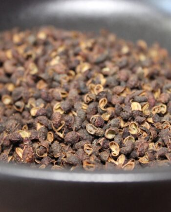 Gros plan sur des grains de poivre de Sichuan dans un récipient noir, offrant une saveur unique et épicée.