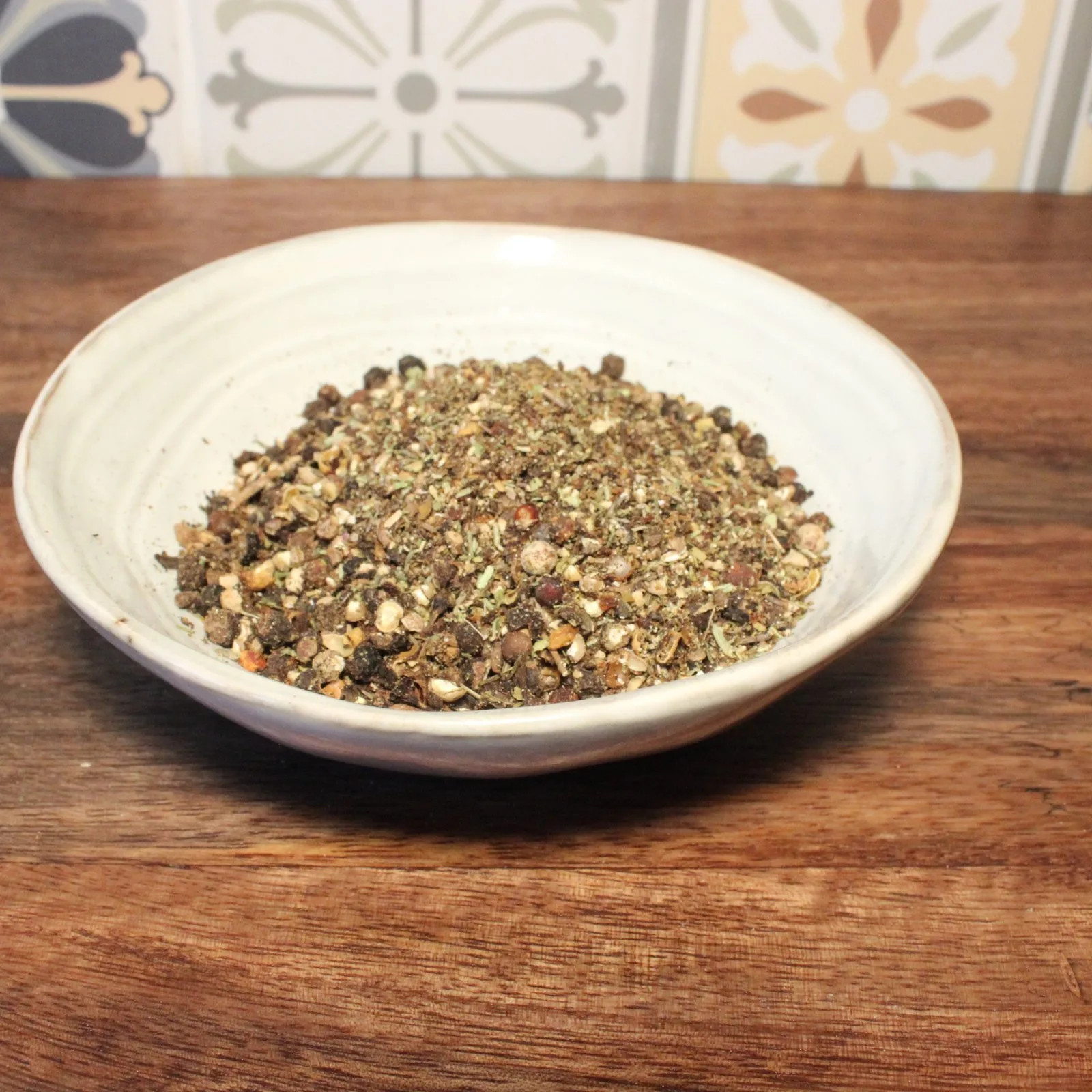 Bol de mélange d'épices sur table en bois, fond de carreaux colorés.