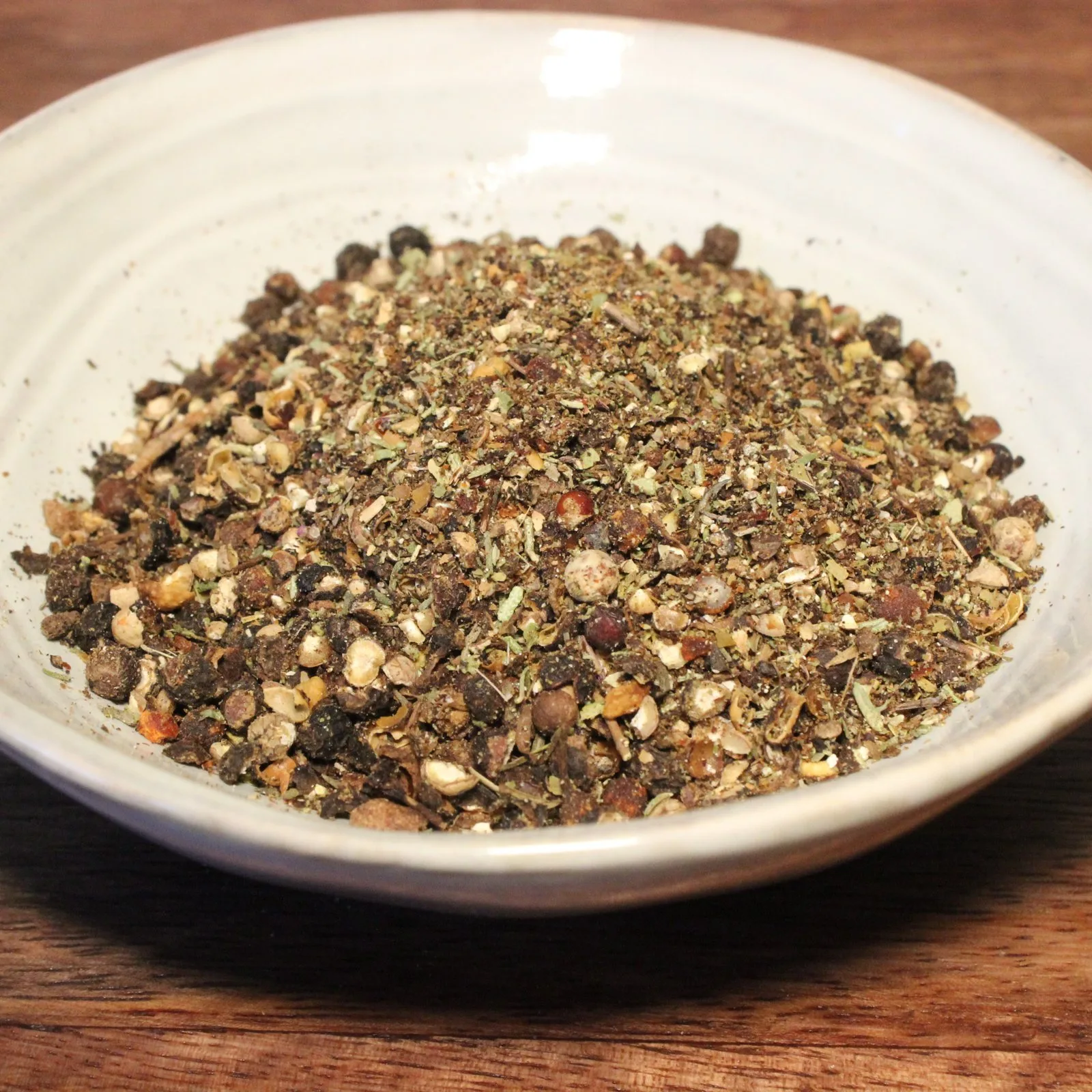 Assortiment de fines herbes et épices séchées dans un bol blanc sur une table en bois.