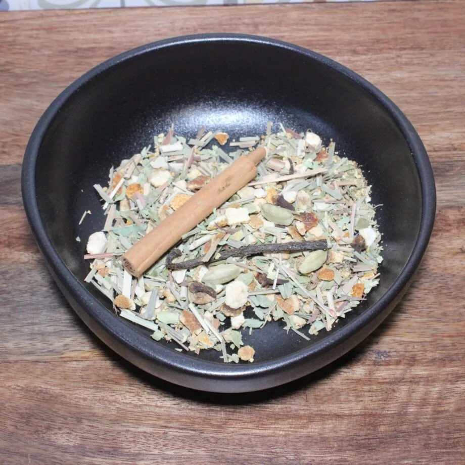 Bol dépices diverses sur une table en bois incluant une branche de cannelle cardamome et herbes séchées