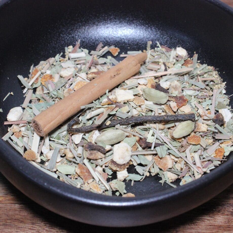 Mélange dépices séchées dans un bol noir avec bâton de cannelle et cardamome pour infusion parfumée