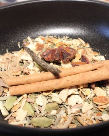 Mélange d'épices variées dans une poêle noire, incluant cannelle et cardamome pour une recette parfumée.