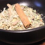 Bol de mélanges d'herbes et épices, incluant un bâton de cannelle pour infusion ou décoration culinaire.