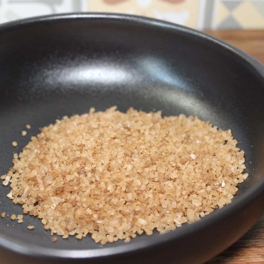 Cristaux de sel brun dans un bol noir sur une table en bois gros plan sur un condiment naturel et rustique