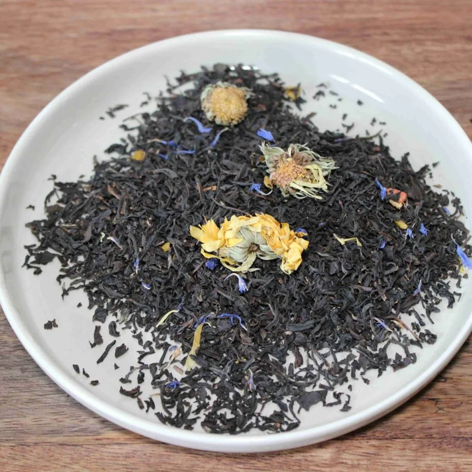 Assortiment de thé noir avec fleurs séchées dans une assiette blanche sur une table en bois