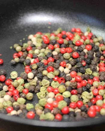 Mélange coloré de grains de poivre dans une poêle, idéal pour rehausser les plats avec une touche épicée et aromatique.