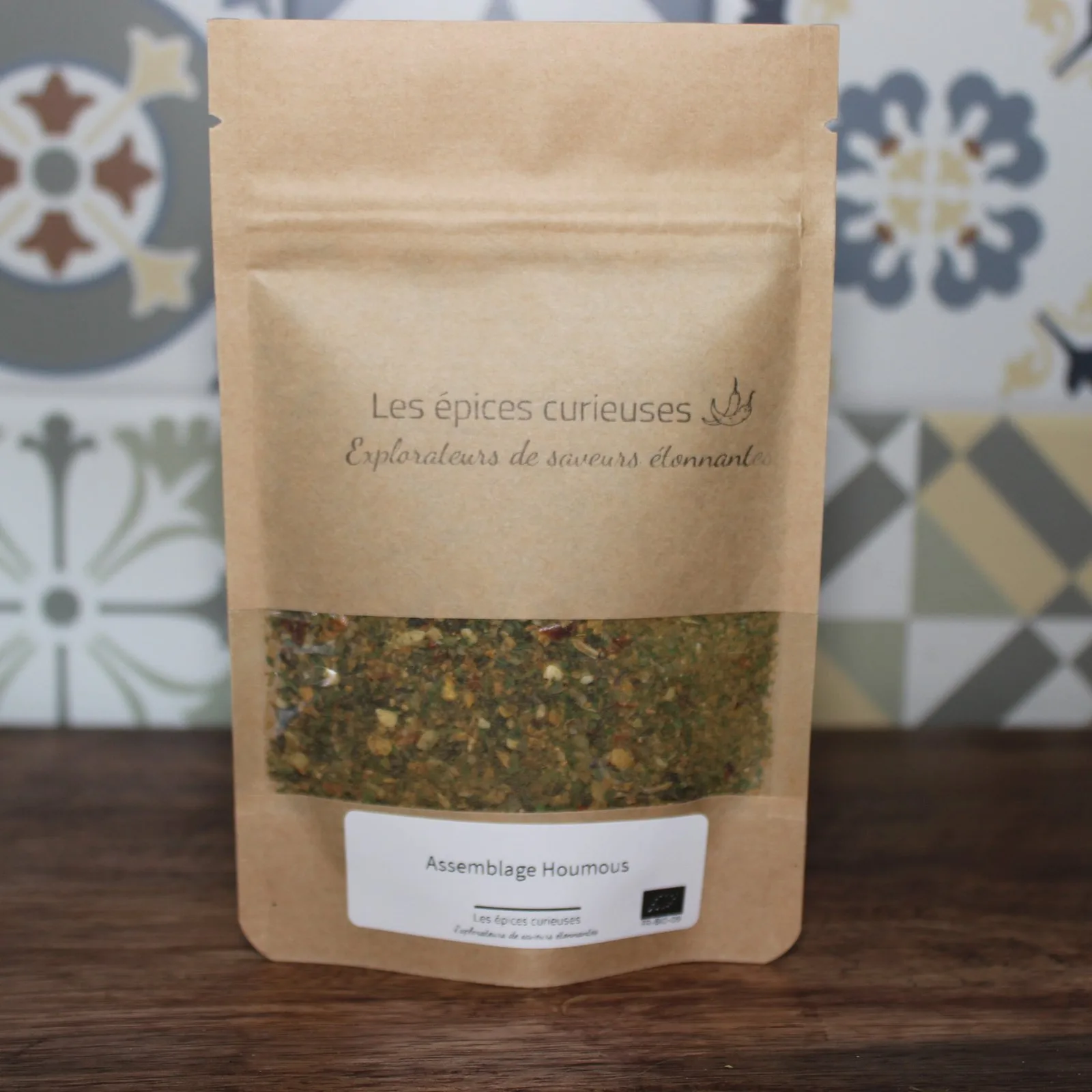 Mélange d'épices houmous par Les Épices Curieuses dans un sachet kraft, devant un fond décoratif.