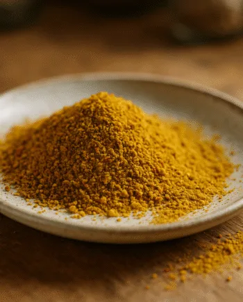 Assiette en céramique avec poudre de curcuma dorée, sur une table en bois rustique.