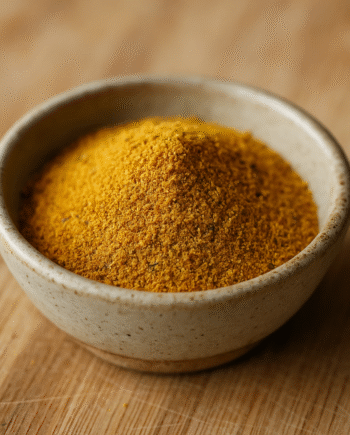 Bol de poudre de curry jaune sur planche en bois, épice exotique pour plats savoureux.