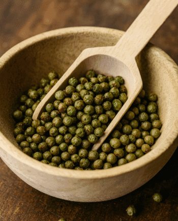 Boulettes de poivre vert dans un bol en bois avec une cuillère, détail de cuisine épicée.