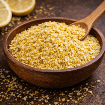 Bol de boulghour doré avec cuillère en bois et tranches de citron en fond sur une table rustique.