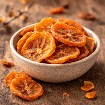 Tranches d'oranges séchées dans un bol en céramique sur une table en bois, parfaites pour un encas sain et gourmand.