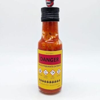 Bouteille de sauce piquante extrême avec étiquettes de danger et avertissements. Usage réservé aux amateurs de piments forts.