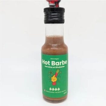 Sauce piquante Hot Barbe à la verveine et rhubarbe dans une bouteille avec étiquette verte et illustration de barbecue.